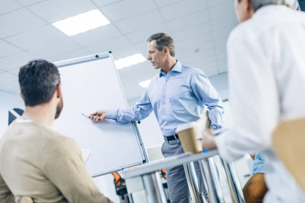 istock Gray-haired man pointing with a pen on flipchart indoors 1132768238