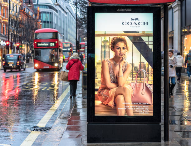 Bus Stop advertisement on rainy London Street London, UK - An advertisement for the fashion brand Coach on an Oxford Street bus stop, as a woman waits for a bus, and other pedestrians pass on the pavement. london fashion stock pictures, royalty-free photos & images