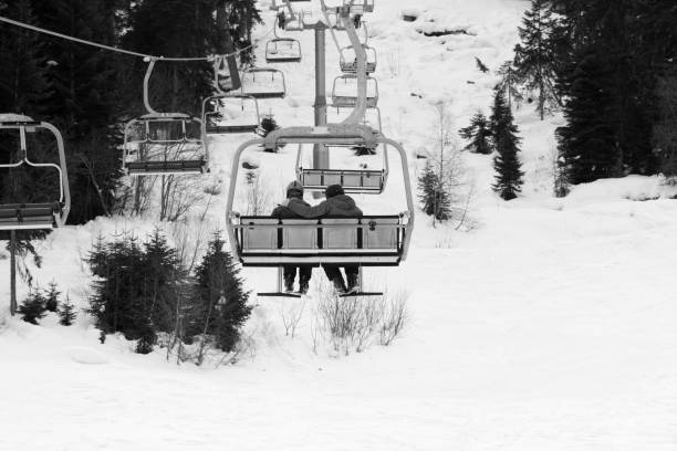Two skiers on chair-lift in gray day Two skiers on chair-lift in gray day. Caucasus Mountains at winter. Hatsvali, Svaneti region of Georgia. Black and white toned landscape. ski lift photos stock pictures, royalty-free photos & images