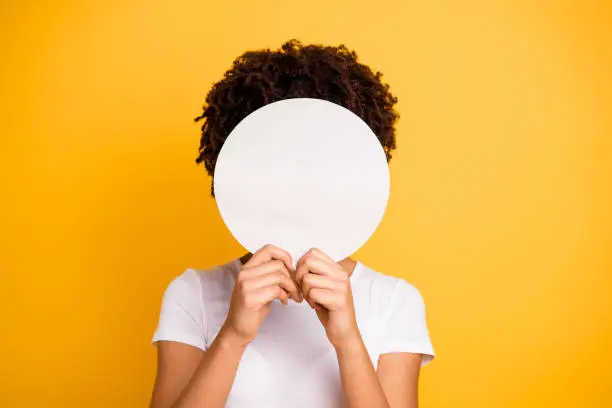 Photo of Close up photo beautiful amazing she her dark skin lady hiding face round circle banner placard do not want be recognized wear casual white t-shirt isolated yellow bright vibrant vivid background
