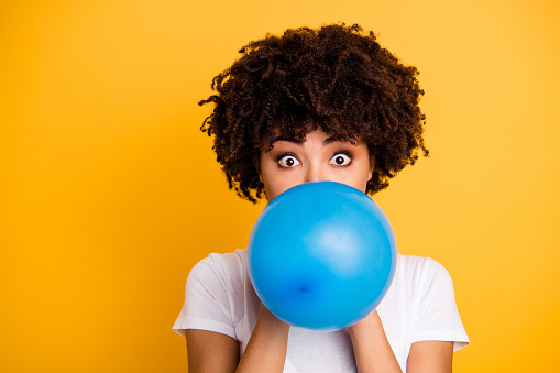 Close up photo beautiful amazing she her dark skin lady hold air balloon eyes surprised stupor hiding face big eyes wear casual white t-shirt isolated yellow bright vibrant vivid background.