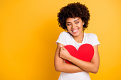 Close up photo beautiful amazing she her dark skin lady adorable remember cuddle big paper card heart shape figure form dreamy wear casual white t-shirt isolated yellow bright vibrant background