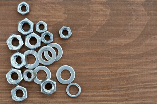 Several various metal fasteners for construction. Nuts, washers and washer-grover, close-up on a wooden background.