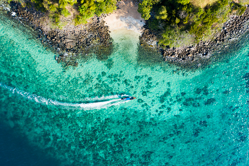 Vista desde arriba, vista aérea de un barco tradicional de cola larga navegando cerca de una impresionante barrera de arrecifes con una hermosa playa pequeña bañada por un mar transparente y turquesa. Isla Phi Phi, Tailandia. photo