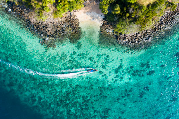 view from above, aerial view of a traditional long-tail boat sailing near a stunning barrier reef with a beautiful small beach bathed by a transparent and turquoise sea. phi phi island, thailand. - phi imagens e fotografias de stock