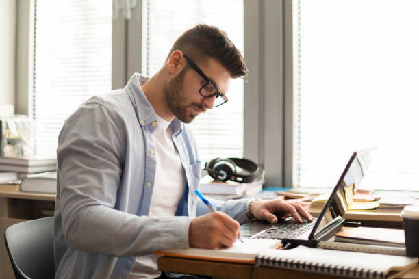 istock Young man in library on laptop 1132786435