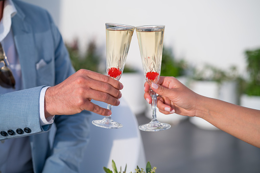 closeup hands of newlywed couple with glasses of sparkling wine cheering outside on restaurant porch