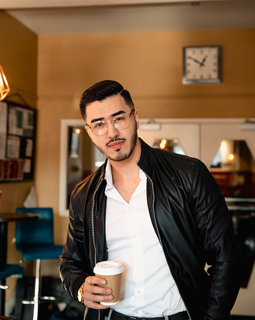 Portrait of a young asian man looking at the camera and smiling. He is holding a cup of coffee to take away.