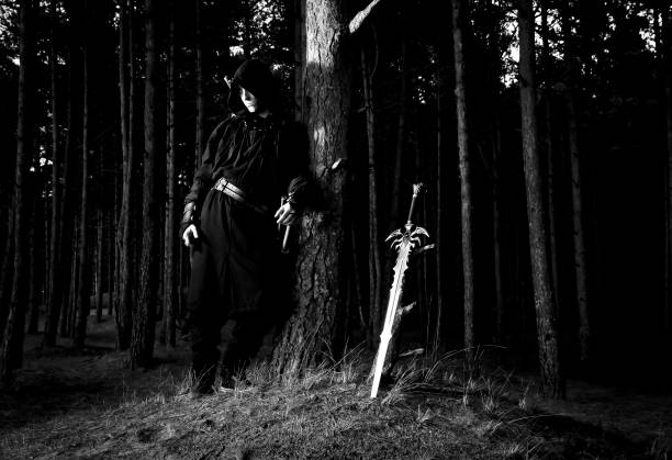 istock Man in assassins suit and sword standing in the forest. 1132790728