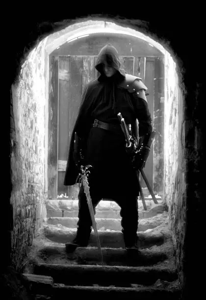 Warrior standing in forgotten and ruined fortress. Black suit, sword with him. He is standing on the stairs.