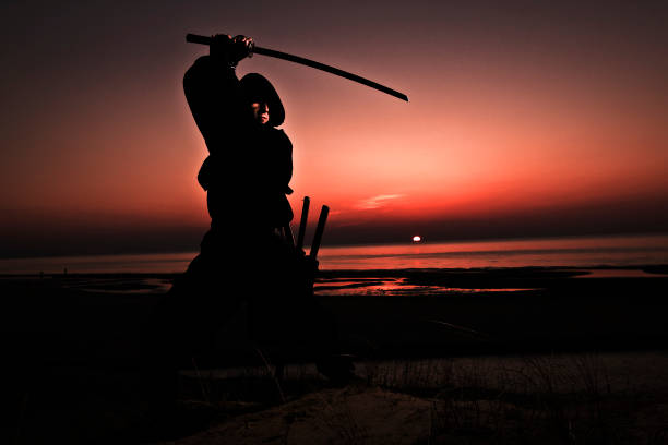 istock Assassin in black suit with sword working out at the beach. 1132790790