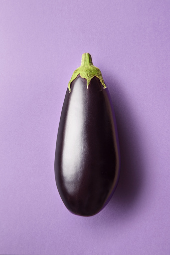 Whole eggplant on a purple background viewed from above. Top view of an aubergine. Copy space