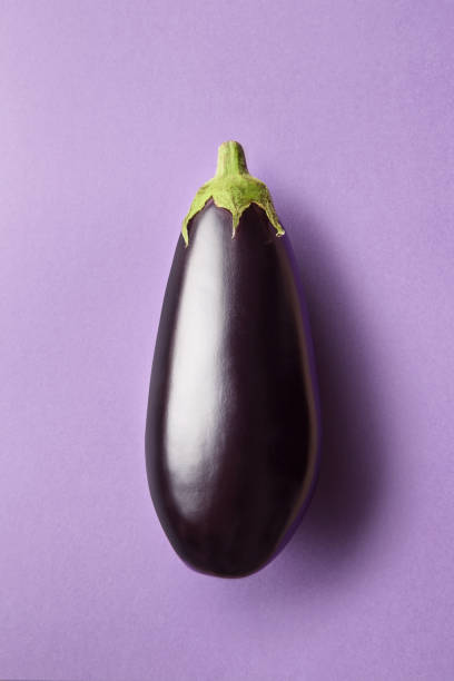 Whole eggplant on a purple background viewed from above. Top view of an aubergine. Copy space stock photo