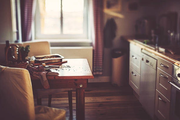 Empty wooden table with free space for product montage or mockup and chair against blurred white kitchen with cutting board and brick wall in scandinavian style in morning light. Copy space.
