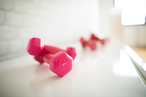 Close up to small pink dumbbells on  white shelf at gym