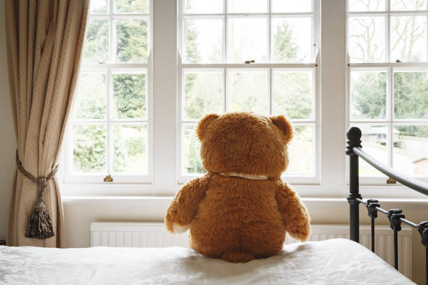 Depression and anxiety Teddy bear sitting on a bed looking out of a window. Can depict loneliness, depression or anxiety man with teddy bear stock pictures, royalty-free photos & images
