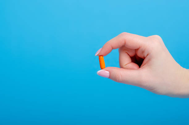 оранжевые таблетки капсулы в руке фармацевтической medecine - фармацевтической стоковые фото и изображения