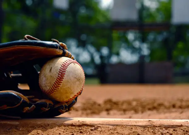 Baseball in glove laying on pitcher's mound of ball field.  Old used sports equipment for team sport.