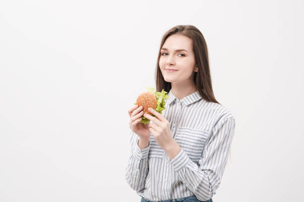 Young beautiful brunette girl on a white background with a hamburger in her hands.