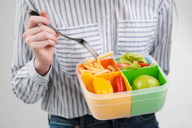 istock Slender brunette girl with long hair on a white background eats with a fork from a container for lunches. Color box for food, a selection of different products and a comprehensive lunch. 1132801842
