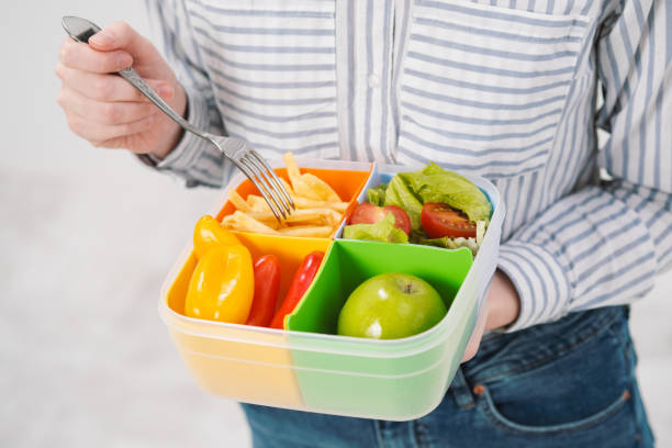 istock Slender brunette girl with long hair on a white background eats with a fork from a container for lunches. Color box for food, a selection of different products and a comprehensive lunch. 1132802709