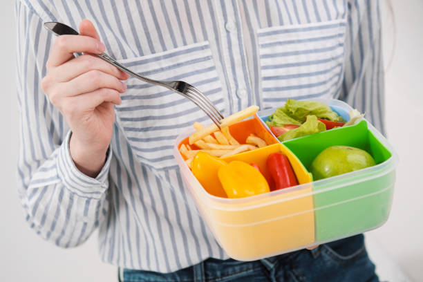 istock Slender brunette girl with long hair on a white background eats with a fork from a container for lunches. Color box for food, a selection of different products and a comprehensive lunch. 1132802808