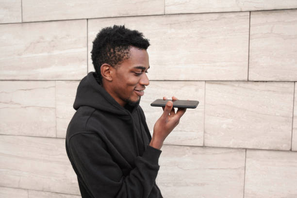 istock portrait smiling african man holding in hands smartphone using voice command recorder, assistant or calling, looking at phone walking on city street on gray wall background 1132804976