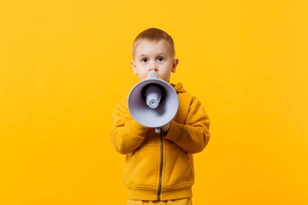 Little fun kid boy 3-4 years old in yellow clothes holding, speaking in electronic megaphone isolated on orange wall background, children studio portrait. People childhood concept. Mock up copy space pequeño niño divertido niño 3-4 años de edad en la tenencia de ropa amarilla, hablando en megáfono electrónico aislado en fondo de pared naranja, retrato de estudio de los niños. concepto de la niñez de la gente. maqueta de espacio de copia.