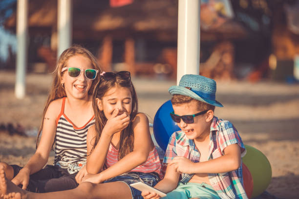 istock Kids laughing watching funny video on smartphone on sandy beach 1132808116
