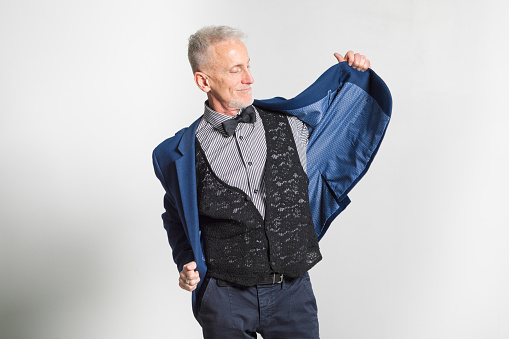 Mature man putting on his jacket smiling. Studio shot on a gray background.