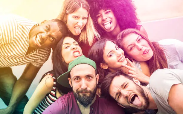 Photo of Multiracial millenial friends taking selfie with funny faces - Happy youth friendship concept against racism with international young trendy people having fun together - Psychedelic radial filter