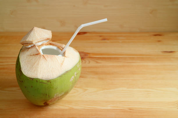 istock Fresh young coconut with white straw isolated on light brown wooden table 1132830771