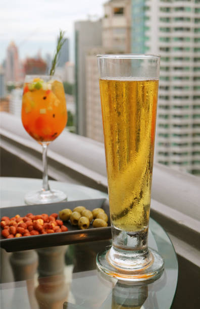 Glass of cold draft beer with blurry fresh fruits Sangria cocktail on round glass table at the roof top bar's terrace