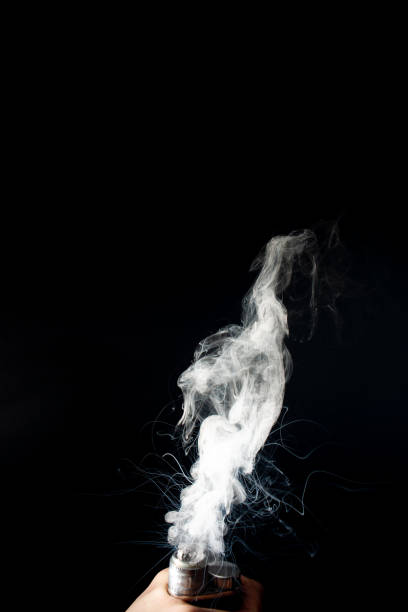 istock Male hand holds vape without atomiser. Column of vape clouds splash from coil on black background. Fog is white. Stock isolated white smoke with spray boiling glycerine. 1132834057