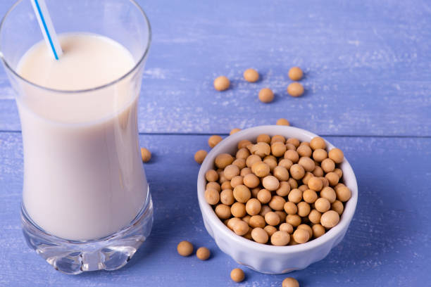 soybeans, and soy milk in the glass in the foreground on the table in light blue wood, yellow soy beans and soy milk in the glass in the foreground bicchiere stock pictures, royalty-free photos & images