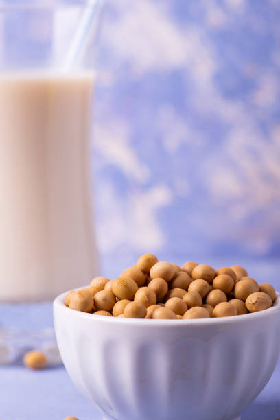 soybeans, and soy milk in the glass in the foreground on the table in light blue wood, yellow soy beans and soy milk in the glass in the foreground bicchiere stock pictures, royalty-free photos & images