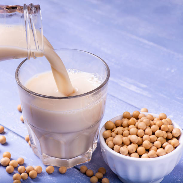 soybeans, and soy milk in the glass in the foreground on the table in light blue wood, yellow soy beans and soy milk in the glass in the foreground bicchiere stock pictures, royalty-free photos & images