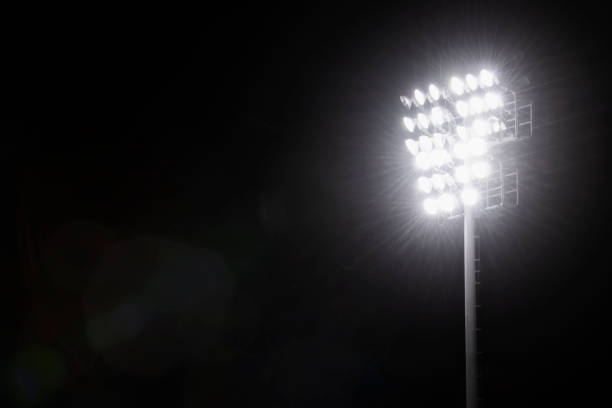 A group of Sports stadium lights atop a pole at night A group of glowing high intensity lamps to illuminate a sports field atop a steel pole at night with insects flying around against a black sky floodlight stock pictures, royalty-free photos & images