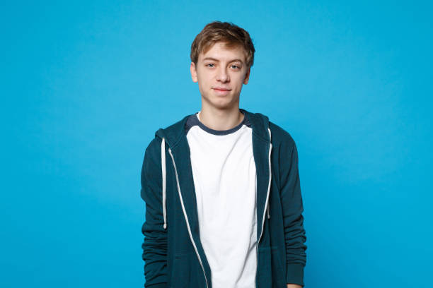 Portrait of attractive handsome young man in casual clothes standing isolated on blue wall background in studio. People sincere emotions, lifestyle concept. Mock up copy space. Advertising area. Portrait of attractive handsome young man in casual clothes standing isolated on blue wall background in studio. People sincere emotions, lifestyle concept. Mock up copy space. Advertising area teenage boys stock pictures, royalty-free photos & images