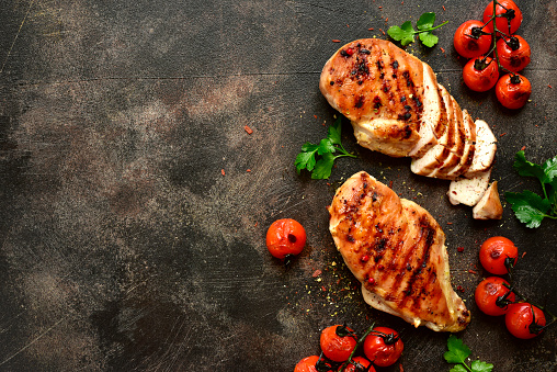 Grilled chicken breasts with roasted tomatoes on a dark slate, stone, metal or concrete background.Top view with copy space.