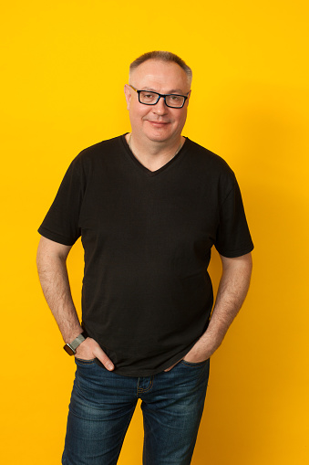 Retrato de estudio de 50 años de edad calvicie hombre en gafas, jeans y camiseta negra sobre fondo amarillo photo