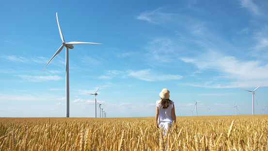 Beautiful girl on yellow field of wheat with windmills for electric power production