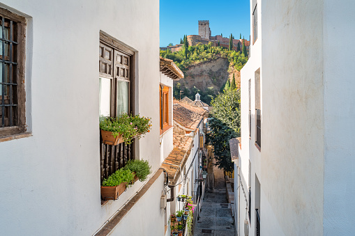 Stock photograph of an alley with whitewashed homes in the medieval Moorish Albaicin district of old town Granada Andalusia Spain with the Alhambra Alcazaba in the background.