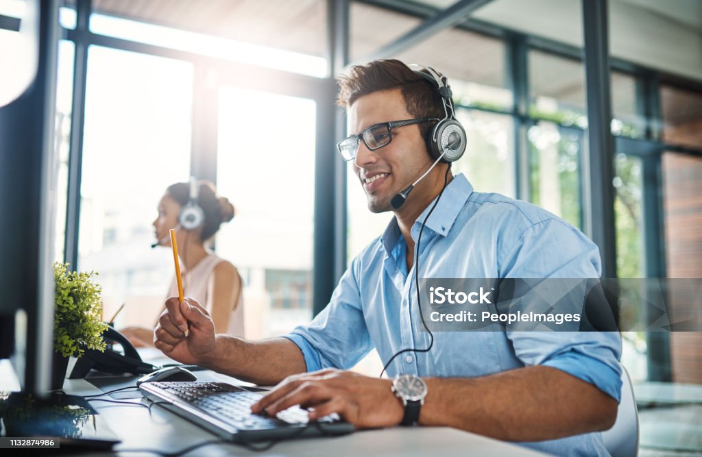 They've got the answers you're looking for Cropped shot of a handsome young man working in a call center with a female colleague in the background Service Stock Photo