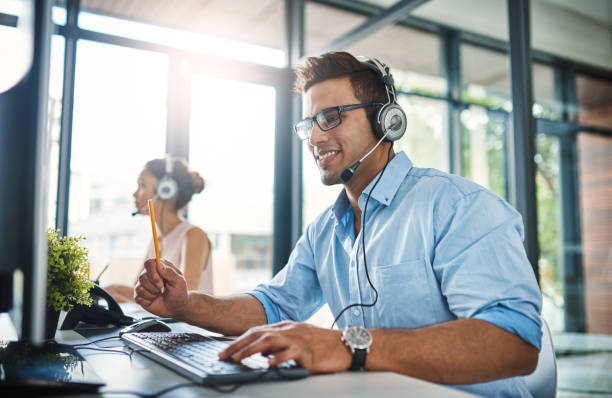 They've got the answers you're looking for Cropped shot of a handsome young man working in a call center with a female colleague in the background service occupation stock pictures, royalty-free photos & images