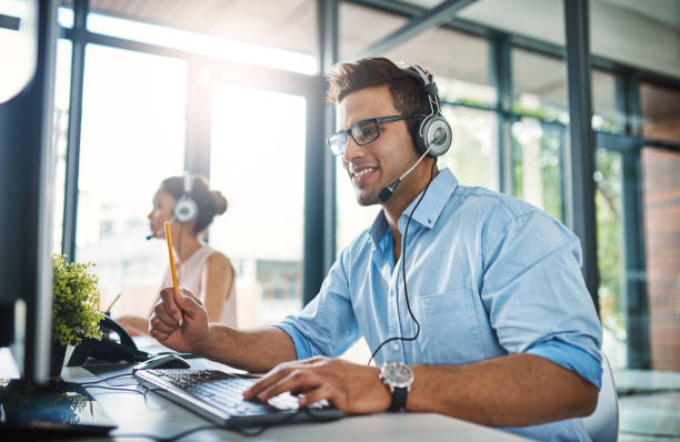 They've got the answers you're looking for Cropped shot of a handsome young man working in a call center with a female colleague in the background customer relationship management stock pictures, royalty-free photos & images