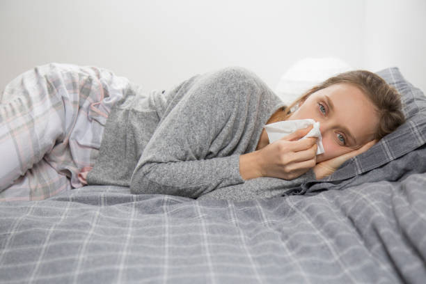 istock Sick woman lying in bed, looking at camera, blowing nose 1132888718