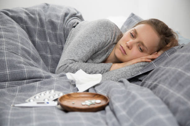 istock Sick young woman lying in bed, looking at pills 1132888737