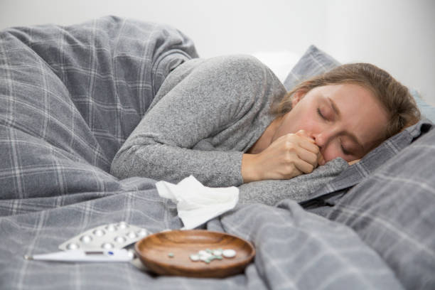 Sick young woman lying in bed with closed eyes, coughing