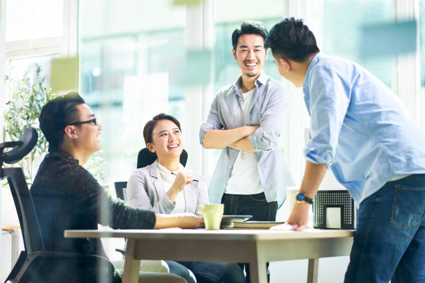 group of young asian business executives talking in office group of four happy young asian corporate people teammates meeting discussing business in office. asian culture stock pictures, royalty-free photos & images
